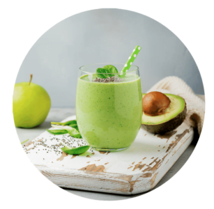 A glass of green smoothie with a green straw, garnished with chia seeds and mint, sits on a white wooden board next to an apple, avocado, and chia seeds—a perfect scene for exploring new smoothie recipes.
