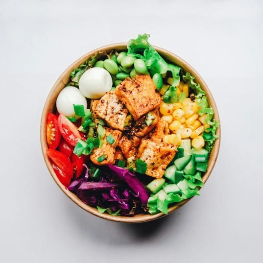 A colorful salad bowl with grilled chicken, tomatoes, purple cabbage, lettuce, cucumbers, edamame, corn, and boiled eggs is a perfect choice to avoid mindset mistakes that often lead to binging.